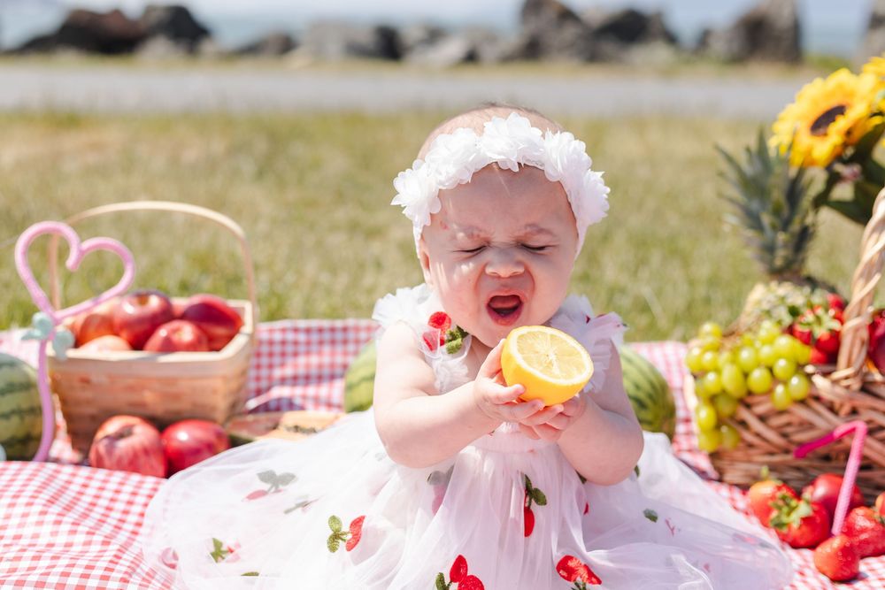 A collection of fresh fruits and picnic items arranged on a red and white checkered blanket outdoors.