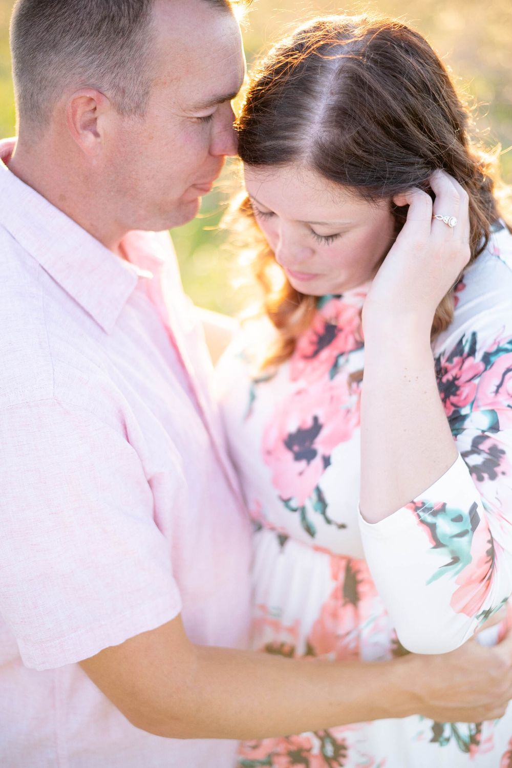 A tender outdoor portrait shows a sweet moment of a couple embracing in soft golden light.