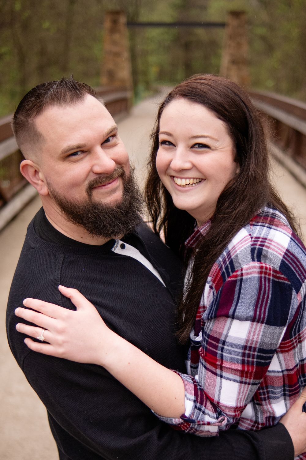 A couple in casual attire share a happy moment together on a wooden bridge in a forest setting.