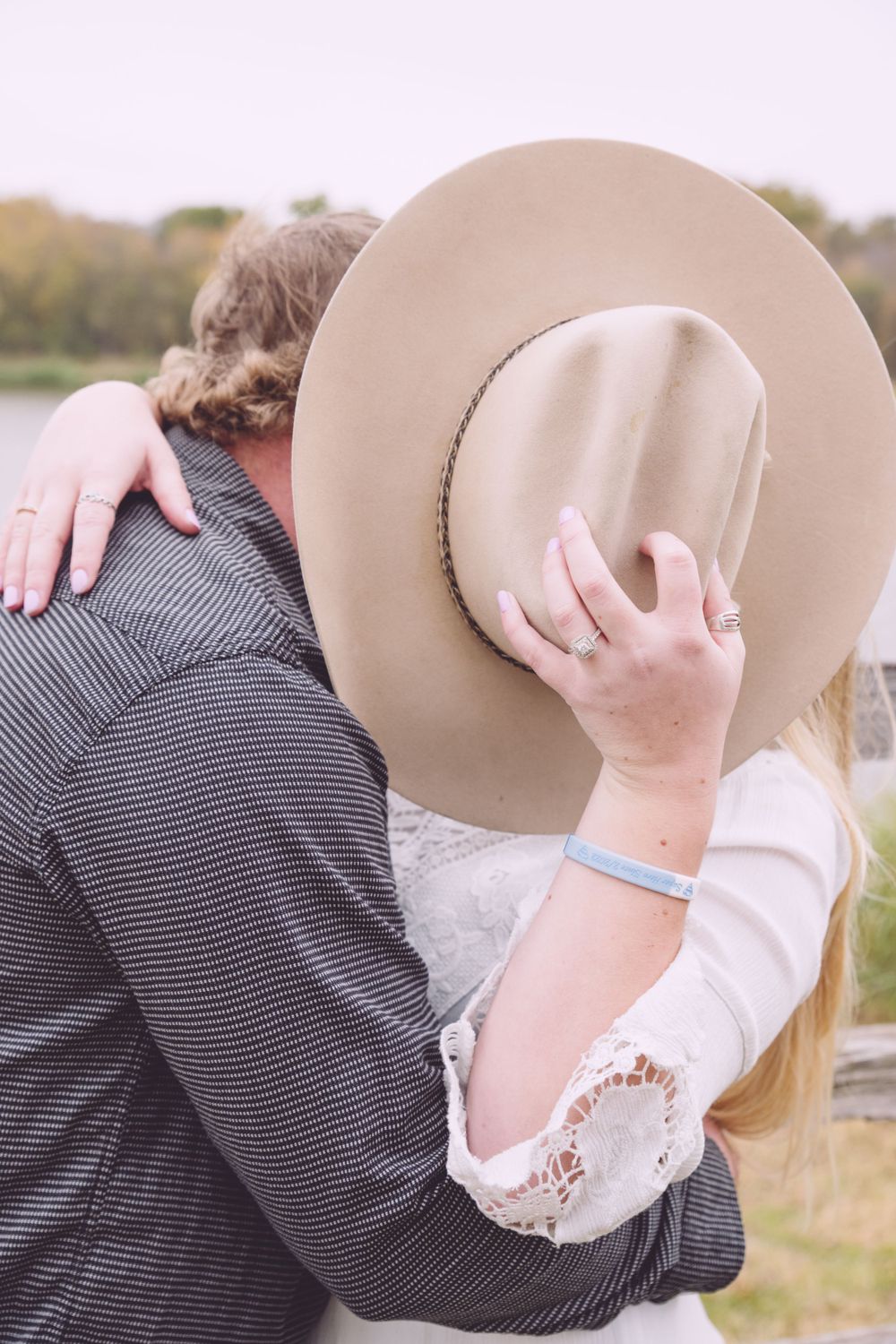 A romantic embrace outdoors with a tan cowboy hat held up to cover the faces in an intimate moment.