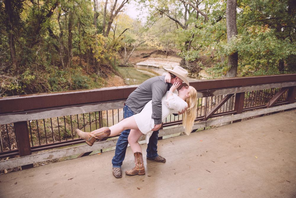 A romantic couple shares an intimate dip pose on a wooden bridge surrounded by autumn trees.