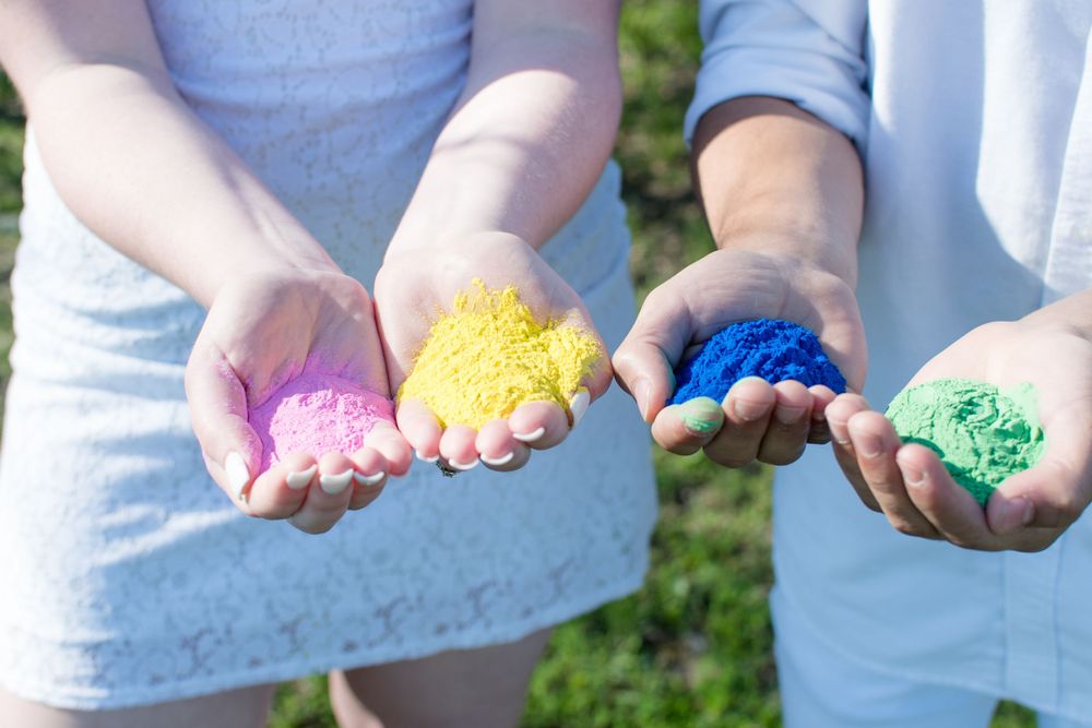 Hands holding colorful powder in pink, yellow, blue and green colors outdoors in sunlight.