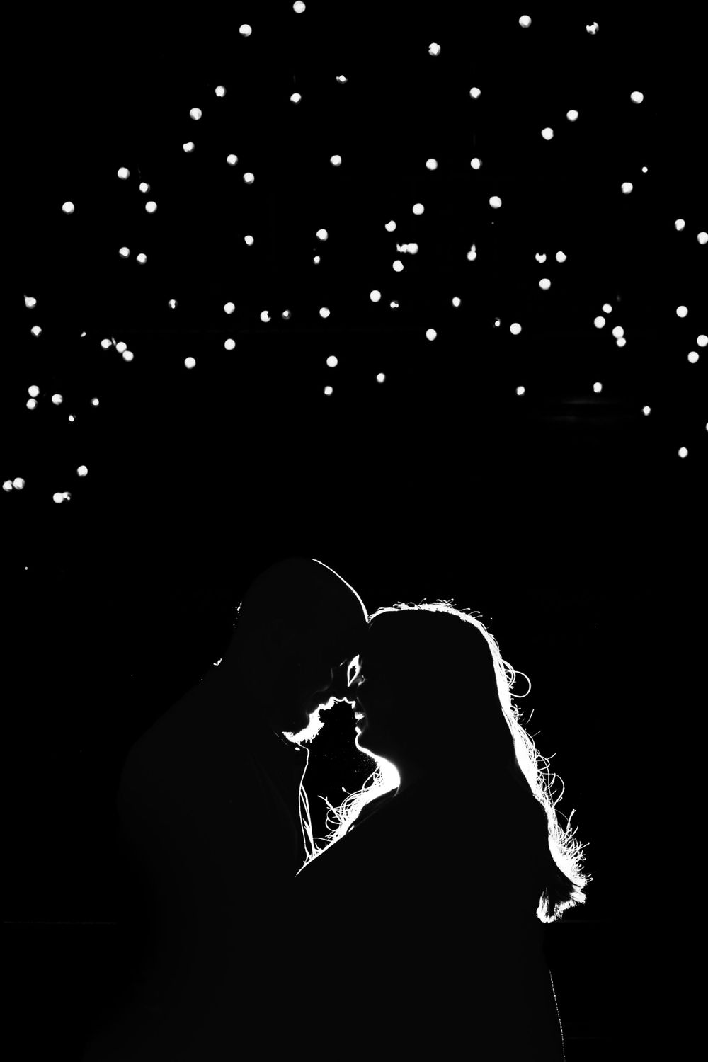 A silhouetted couple shares an intimate moment under twinkling lights in the night sky.