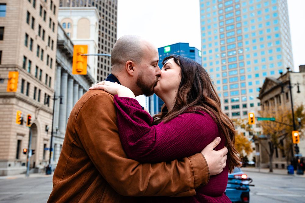 Two people embrace on a city street lined with tall buildings.