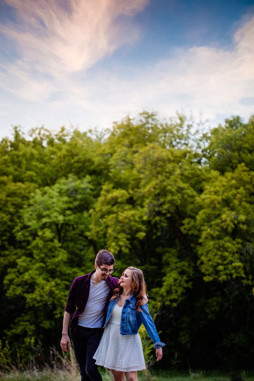 A couple shares a joyful moment in a field at sunset with trees in the background.