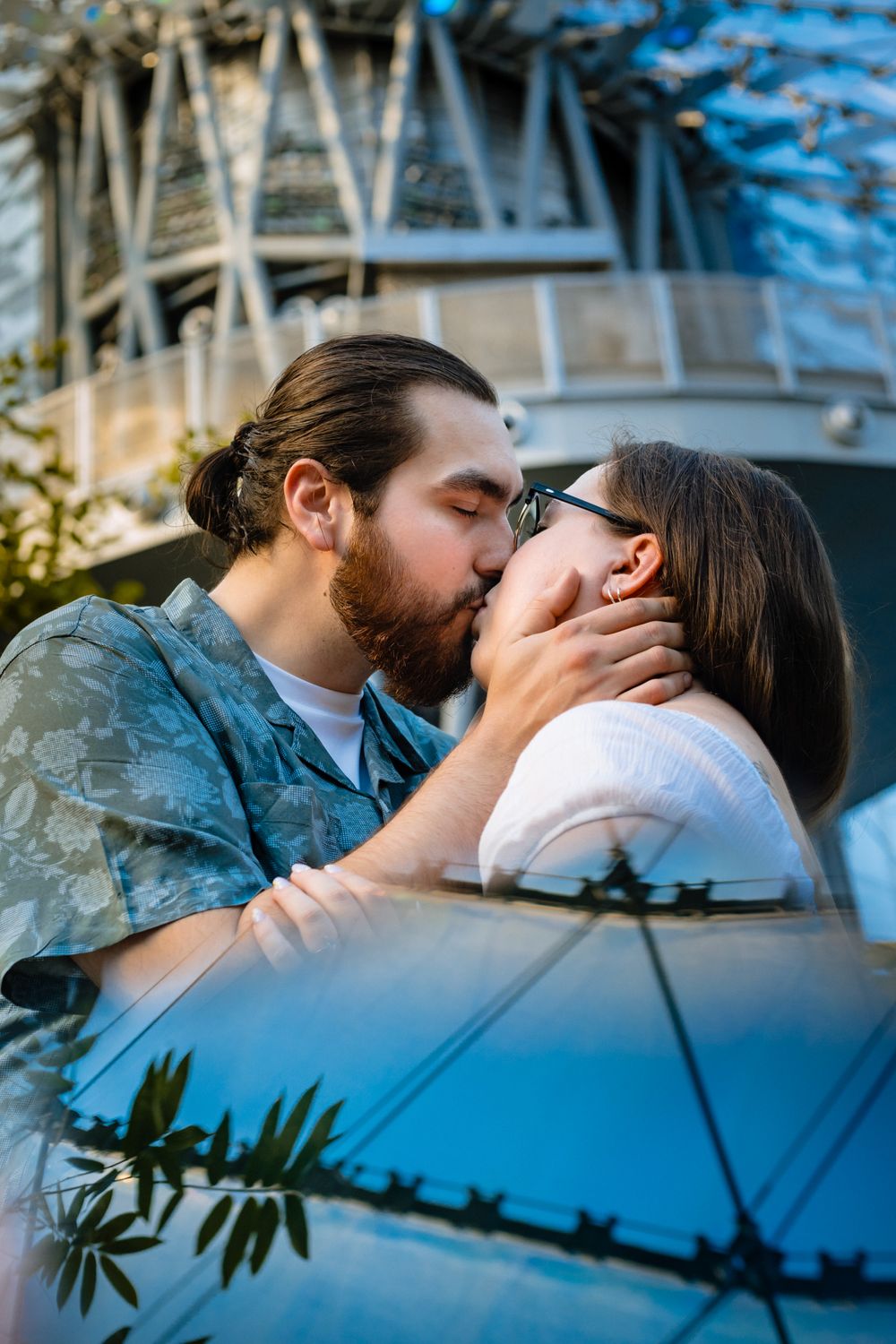 A romantic embrace against a blue car with urban architecture in the background.
