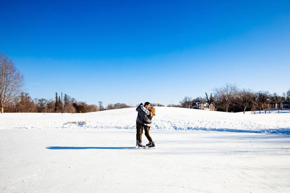 A couple embraces on a snow-covered landscape under bright blue winter skies.