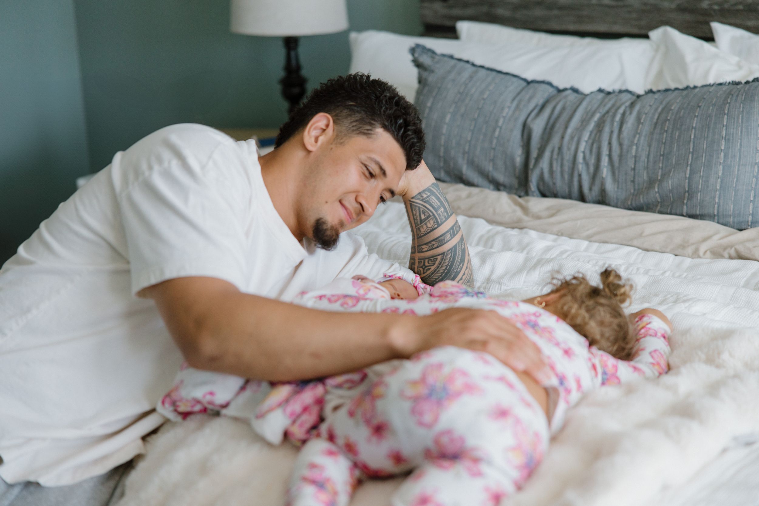 A parent lies on a bed beside a baby wearing pink tie-dye pattern clothing.