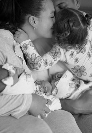 Black and white photo showing tender embrace on white bedding with floral patterned clothing.