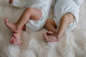 Close up view of tiny baby feet on soft white blanket showing small toes and bare legs.