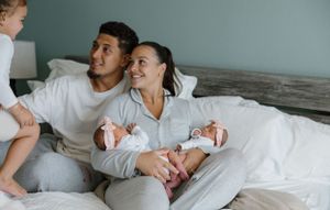A happy couple in gray loungewear relaxes together on a bed with twins in a comfortable home setting.