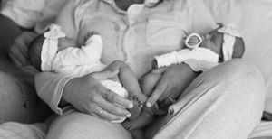 Black and white close-up photograph showing gentle hands holding a baby's tiny feet.