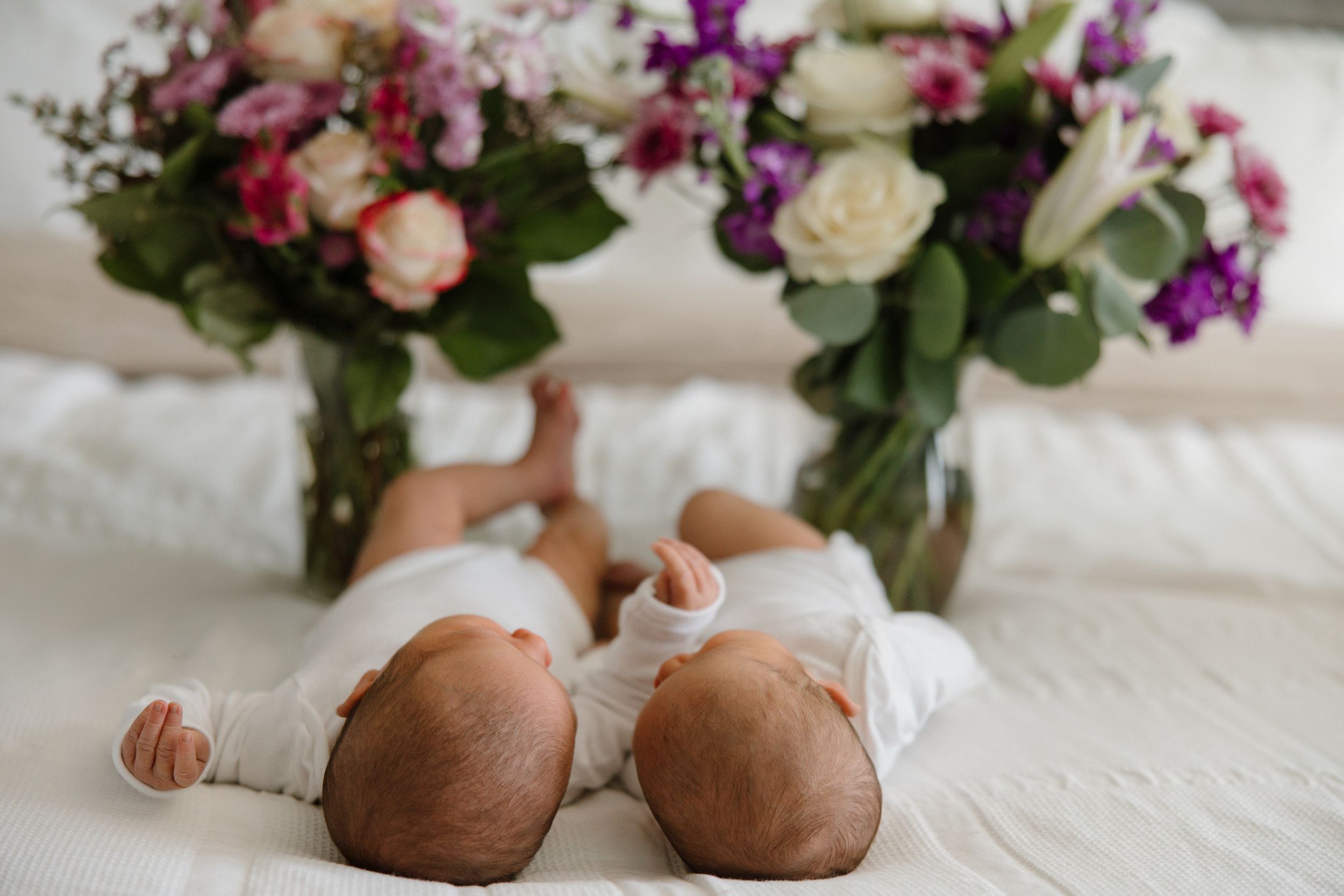 Brown ballet slippers on white textured fabric with colorful floral arrangements in glass vases in the background.
