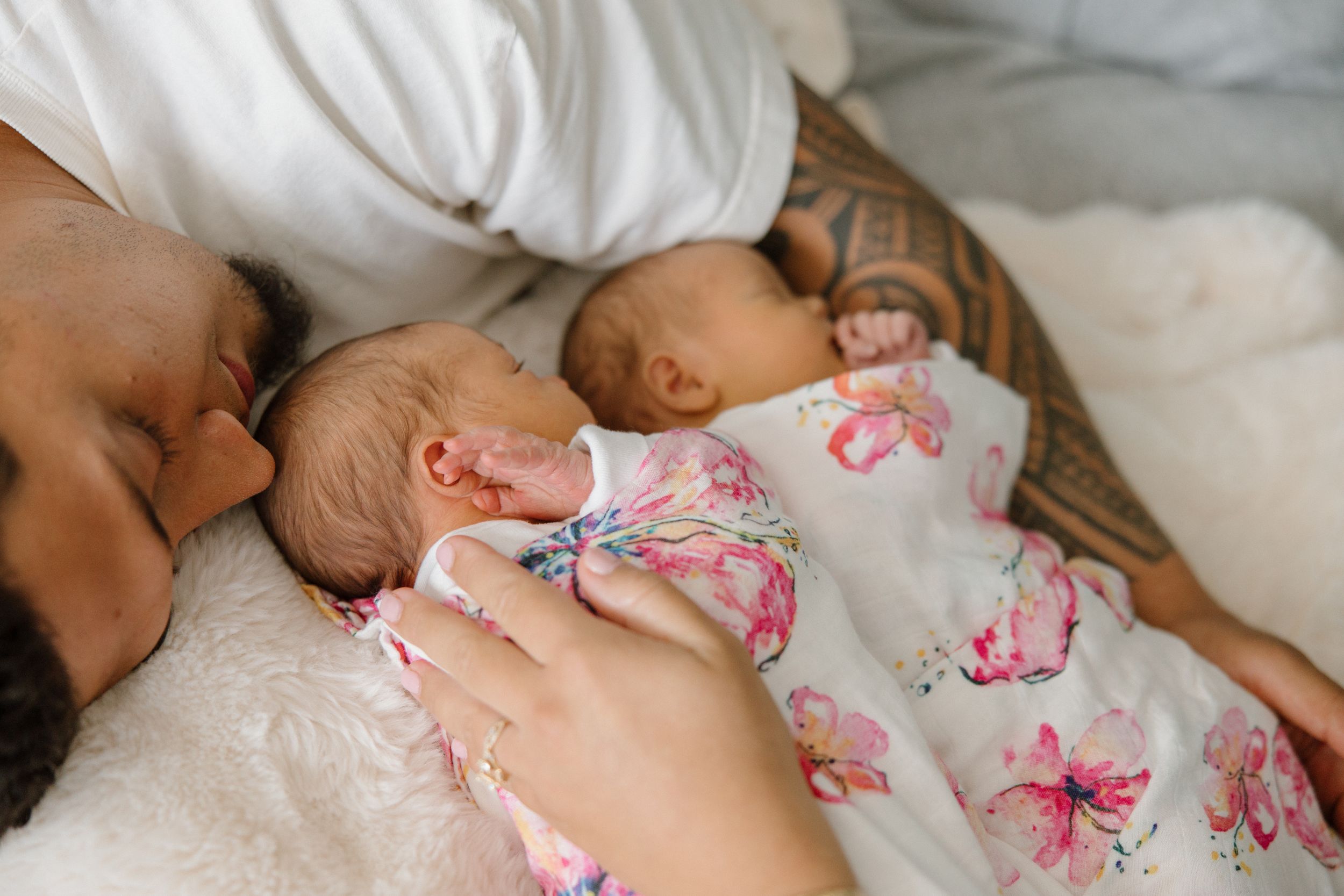 A sleeping baby rests peacefully wearing a white and pink floral outfit on soft bedding.