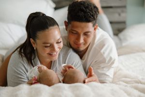 Young couple lying on bed and bonding with their newborn baby in bright bedroom setting.