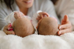 Two sleeping infants on soft white bedding with gentle hands supporting them.