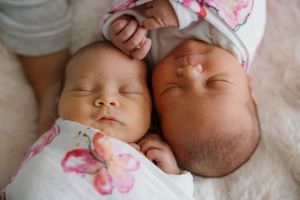 Two sleeping infants in floral outfits resting peacefully side by side on white bedding.