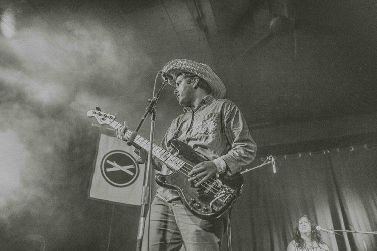 Black and white concert photo of a musician playing guitar on stage with dramatic smoke effects.