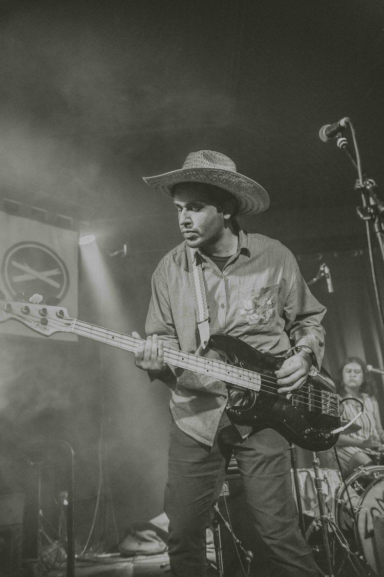Black and white photo of a bassist performing on stage in a hat and casual attire during a live concert.