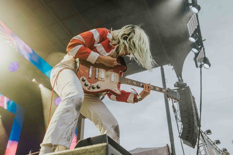 Dynamic low-angle shot of a musician playing guitar during a live performance with colorful stage lighting.
