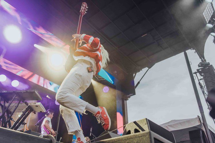 An energetic performer leaps on stage during a concert with dramatic purple lighting and fog effects.
