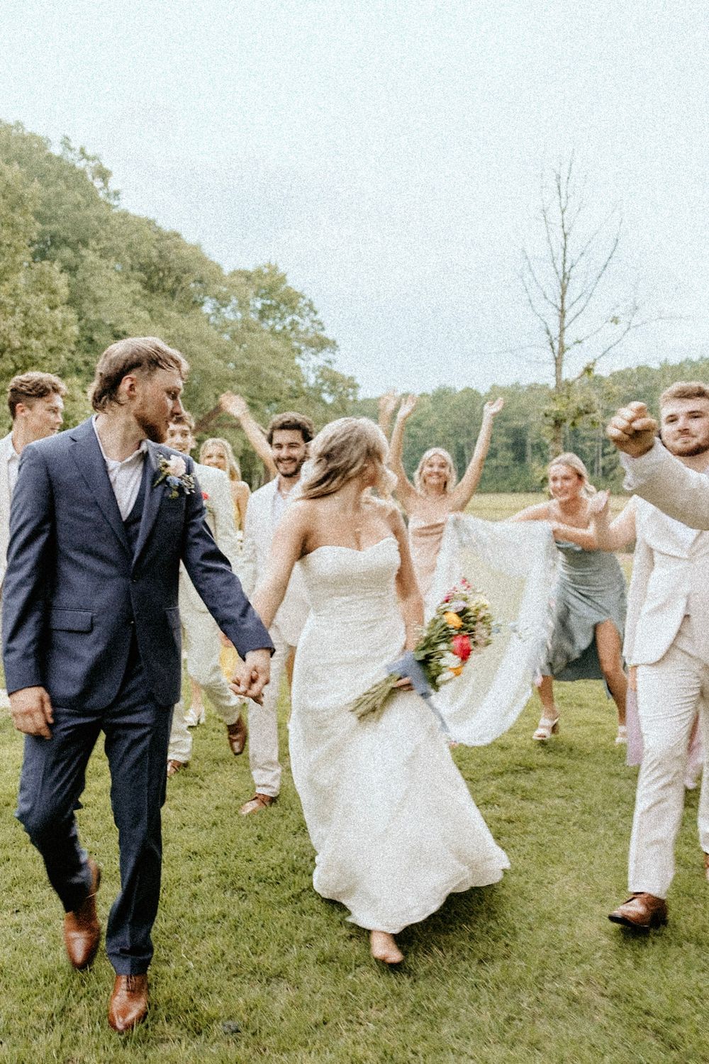 Joyful wedding party celebrates on a grassy lawn as newlyweds dance and laugh together on their special day.