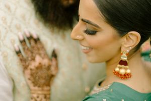 Side profile showing intricate henna art with statement red and gold chandelier earring against a soft blurred background.