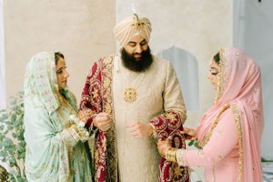 Three people in traditional Indian wedding attire with elegant shawls and embroidered clothing share a moment together.