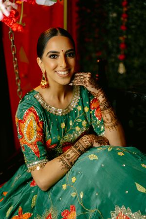 Traditional Indian bridal attire featuring an emerald green lehenga with gold embellishments and intricate henna designs.