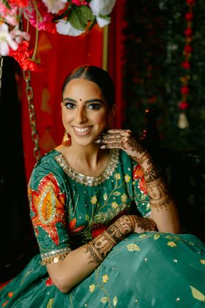 Beautiful traditional Indian bride wearing an emerald green lehenga with intricate henna designs and elegant jewelry.
