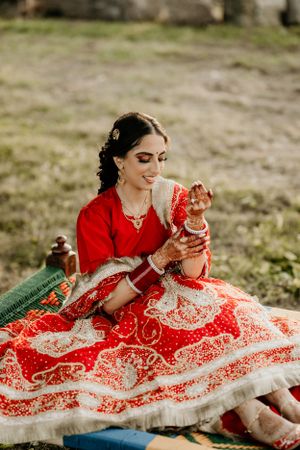 A bride in a stunning red and white embroidered lehenga sits gracefully on the ground during a traditional Indian wedding ceremony.