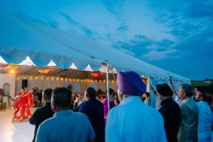 Wedding guests gather under illuminated white tents during an evening outdoor celebration with colorful decorations.