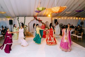 Guests in colorful traditional Indian lehengas and formal attire dancing at a festive wedding reception under white tent decor.