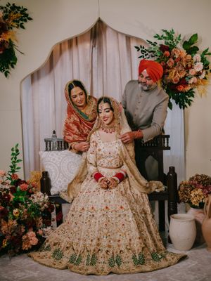 Traditional Indian wedding scene with elaborate cream and gold lehenga, floral decorations and elegant backdrop setup.
