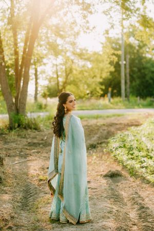 A person in a light turquoise traditional Indian sari stands on a dirt path during golden hour sunset lighting.