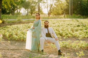 A couple poses outdoors in a sunlit field, wearing formal attire including a mint green gown and white suit.