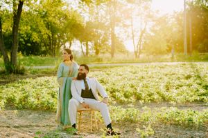 A couple poses in a sun-drenched park during golden hour with yellow wildflowers and trees in the background.
