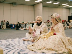 Traditional Sikh wedding ceremony taking place in a large hall with guests seated on the floor.