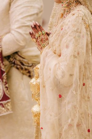 Intricate gold jewelry and embellished cream traditional wedding attire with delicate red floral details.