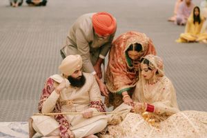 Four people in traditional South Asian wedding attire sit together on a carpeted floor during a ceremony.