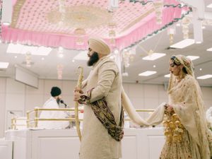 Sikh wedding ceremony taking place under pink decorative ceiling with bride and groom in traditional attire.