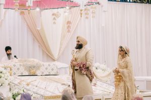 Traditional Sikh wedding ceremony with couple standing at decorated white mandap adorned with floral arrangements.