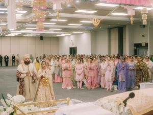 Large Sikh wedding ceremony with guests in colorful traditional attire gathered in a decorated hall.