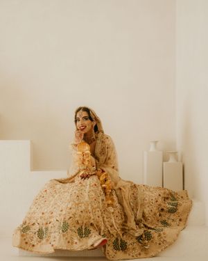 A person in a traditional cream-colored lehenga with intricate embellishments sits gracefully on the floor in a minimalist room.