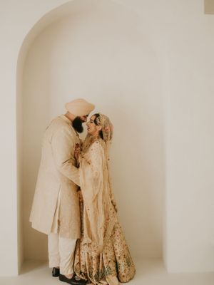 Intimate wedding portrait of couple in traditional Indian attire embracing in minimal white archway.