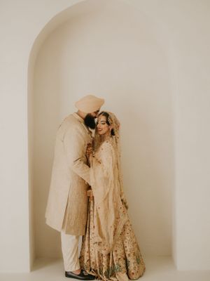 Intimate wedding portrait of couple in traditional Sikh attire standing in white archway.