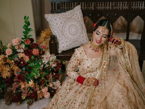 Traditional Indian bridal attire featuring an ornate cream lehenga with floral arrangements in the background.