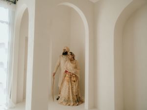 Wedding couple poses elegantly in white arched alcove wearing traditional South Asian wedding attire.