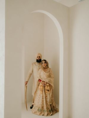 Wedding couple in traditional Indian attire stand beneath minimalist white archway.