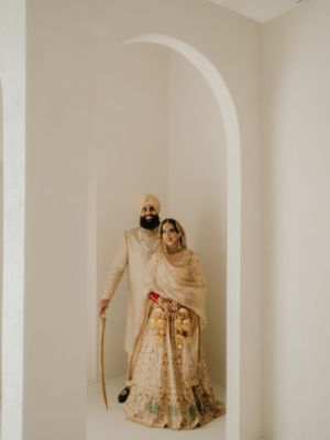 Elegant wedding couple in traditional attire pose in minimalist white arched doorway.